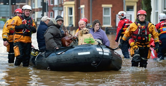 Several elderly people are sitting on a raft, being helped through a flooded town my emergency workers.
